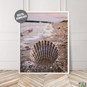 以下が含まれることがあります： 泡立つ波が打ち寄せる砂浜に置かれた貝殻のクローズアップ。貝殻は茶色と白で、表面はざらざらしている。背景はぼやけた海と空の画像である。