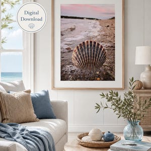 May include: A framed wall art print featuring a photograph of a single ridged seashell resting on a sandy beach at the water's edge, with a soft pink and blue sky in the background. The image includes a circular badge with the text Digital Download.