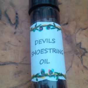 May include: A small, dark brown glass bottle with a black cap and a white label that reads "Devils Shoestring Oil". The label has a green vine border with yellow and red flowers.