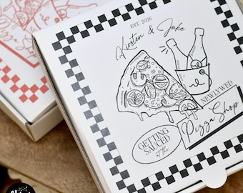 Może przedstawiać: Białe pudełko na pizzę z czarno-białą szachownicą. Pudełko zawiera ilustrację kawałka pizzy, butelki szampana oraz tekst "Kirsten & Jake" i "Pizza Shop". Pudełko zawiera również tekst "Getting Sauced at the Newlywed".