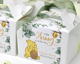 May include: White favor boxes with a Winnie the Pooh theme. Each box features a yellow Winnie the Pooh illustration, a honey pot, and the text "A little Hunny is on the way". Green ribbon and eucalyptus leaf accents complete the design.