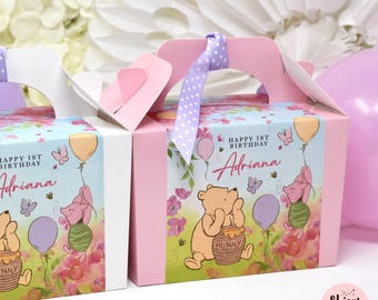 May include: Pink party favor boxes with handles, featuring illustrations of Winnie the Pooh, Piglet, balloons, and flowers. The boxes are decorated with the text "Happy 1st Birthday Adriana". A purple ribbon with white polka dots is tied on top.