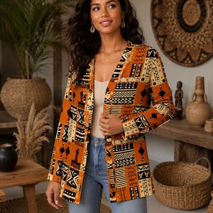 May include: A long-sleeved blazer in a vibrant orange hue, featuring a repeating geometric pattern in black and cream. The garment has a V-neckline, a button-down front closure, and a structured fit, paired with light blue denim jeans.