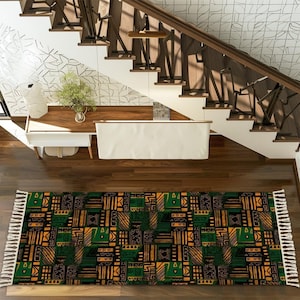 Peut inclure: Tapis rectangulaire avec un motif géométrique vert, noir et or. Le tapis a une frange blanche aux deux extrémités et est posé sur un parquet. Le tapis est devant un escalier.