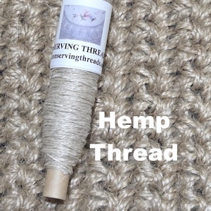 Puede incluir: Una bobina de hilo de cáñamo natural, enrollada alrededor de un núcleo de cartón, con una etiqueta que dice "SERVING THREADS". El texto "Hemp Thread" se muestra en blanco. El hilo es de color beige claro.