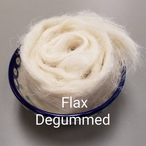 Könnte beinhalten: Ein Wirbel aus entbasteten, cremefarbenen Flachsfasern in einer kleinen Schale mit blauem Rand und weißem Muster. Der Text "Flax Degummed" ist sichtbar. Die Fasern wirken weich und flauschig, ideal zum Basteln.
