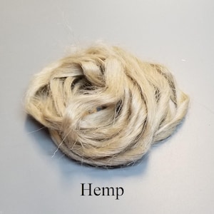 May include: A close-up of a bundle of natural hemp fibres, showing a light beige colour and a slightly coarse texture. The word "Hemp" is printed in black at the bottom of the image.