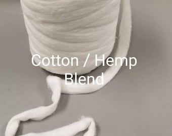 May include: A large, cylindrical spool of white cotton and hemp blend yarn. A length of the yarn extends from the spool, lying on a gray surface. The text "Cotton / Hemp Blend" is displayed on the image.