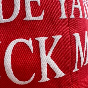 May include: Red baseball cap with white embroidered text. The hat's fabric has a textured appearance. The text on the hat reads "JUCK MA".
