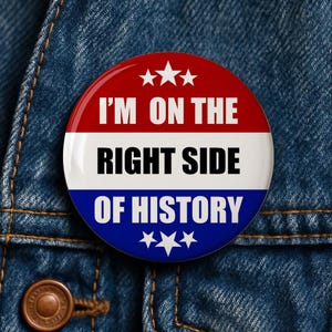 May include: A round button with a red, white, and blue design. The button has the text "I'M ON THE RIGHT SIDE OF HISTORY" in bold white letters. Three white stars are at the top and bottom of the button. The button is on a denim jacket.