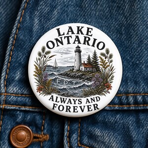 May include: A round pinback button featuring a white background with a detailed illustration of a lighthouse on a rocky shore, a sailboat on the water, and surrounding foliage. The text reads LAKE ONTARIO at the top and ALWAYS AND FOREVER below.