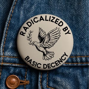 Może przedstawiać: Okrągła, kremowa przypinka z napisem "RADICALIZED BY BASIC DECENCY" otaczającym czarno-białą ilustrację gołębia z gałązką oliwną. Przypinka jest umieszczona na niebieskiej kurtce dżinsowej.