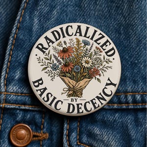 May include: A round pinback button with a cream background featuring a central illustration of a wildflower bouquet wrapped in brown paper. The text RADICALIZED BY BASIC DECENCY is printed in black capital letters around the floral design.