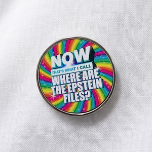 Pode incluir: Um broche circular com um fundo em espiral nas cores do arco-íris e texto em branco que diz: NOW THAT'S WHAT I CALL WHERE ARE THE EPSTEIN FILES? O design inclui uma borda metálica prateada e um acabamento brilhante.