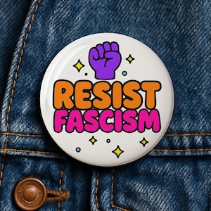 Puede incluir: Un botón blanco con las palabras "RESIST FASCISM" en naranja y rosa, con un puño morado. El botón está decorado con estrellas amarillas y pequeños círculos azules, sobre un fondo de mezclilla.