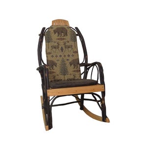 May include: A rustic rocking chair with a natural wood frame and a seat and backrest cushion featuring a forest-themed pattern with bears, deer, and trees. The chair has a curved back and armrests.