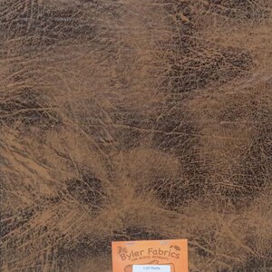 May include: Close-up of a brown faux leather fabric with a distressed, textured look. The fabric is labelled "Byler Fabrics for Rustic Retreats" and "Calf Mocha".