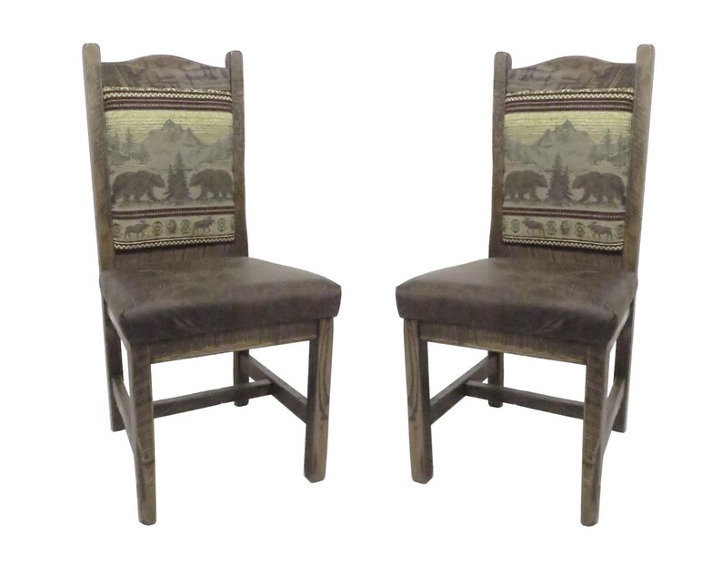 May include: Two wooden chairs with dark brown upholstered seats and high backrests. The backrests feature a woven fabric panel depicting a mountain landscape with bears and trees in shades of brown, green, and tan, set against a dark wood frame.