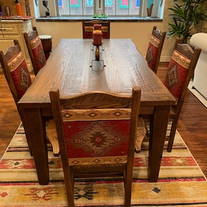 May include: A rustic wooden dining table with six chairs. The chairs have red and brown patterned cushions. The table has a natural wood finish and is surrounded by a patterned rug.