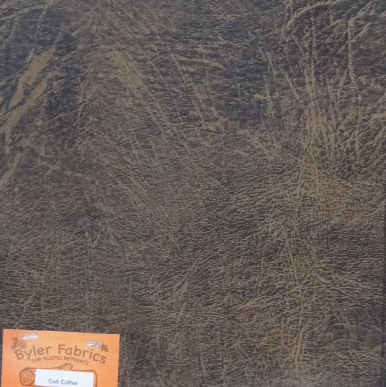 May include: A close-up of a brown faux leather fabric with a textured surface. The fabric is labelled "Colt Coffee" by "Byler Fabrics for Rustic Retreats".