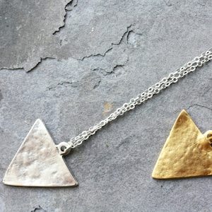 May include: Two silver triangle pendants on chains. One pendant is silver and the other is gold.
