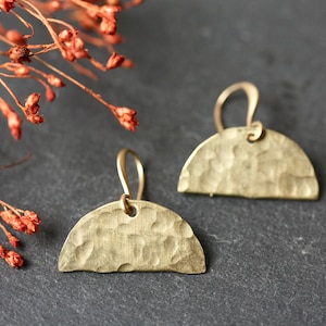 May include: A pair of gold-toned earrings with a hammered half-circle design. The earrings have a simple wire hook fastening.