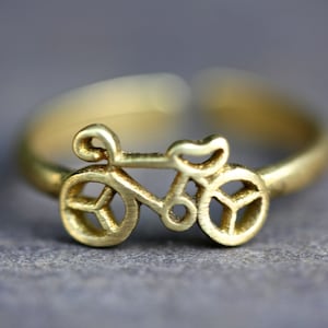 Puede incluir: Un anillo ajustable de metal dorado con un diseño de silueta de bicicleta.