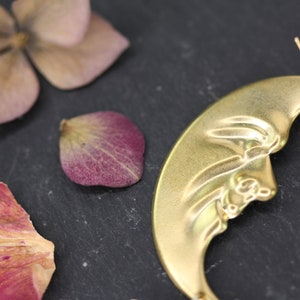 May include: A pair of gold crescent moon earrings with a detailed design. The earrings are made of metal and have a wire hook closure.