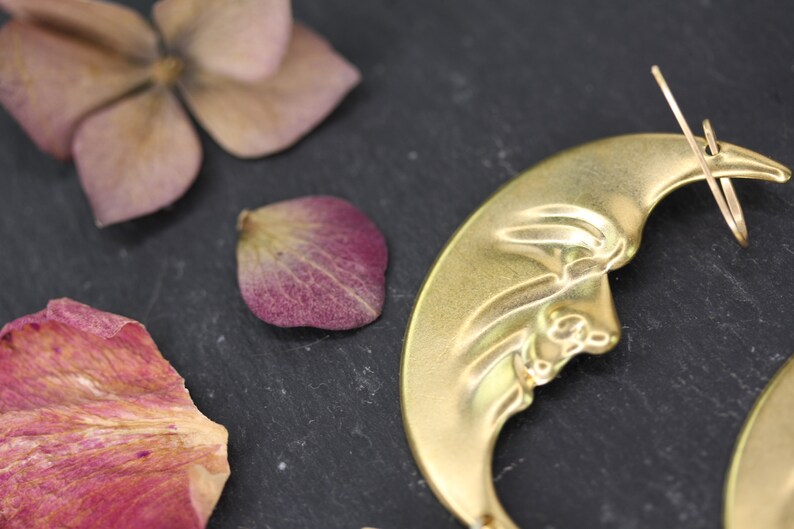 May include: A pair of gold crescent moon earrings with a detailed design. The earrings are made of metal and have a wire hook closure.