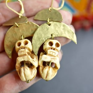 May include: A pair of gold tone earrings with a skull charm and a crescent moon design.