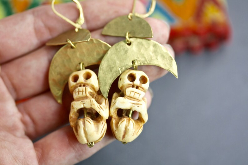 May include: A pair of gold tone earrings with a skull charm and a crescent moon design.