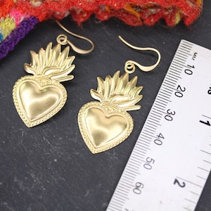 K&ouml;nnte beinhalten: Ein Paar goldfarbene Ohrringe mit einem Herzdesign und einer flammenf&ouml;rmigen Krone. Die Ohrringe sind etwa 5 cm lang.