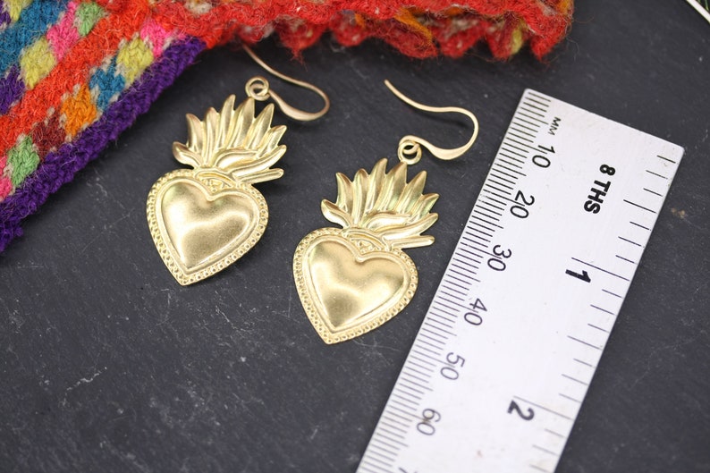 K&ouml;nnte beinhalten: Ein Paar goldfarbene Ohrringe mit einem Herzdesign und einer flammenf&ouml;rmigen Krone. Die Ohrringe sind etwa 5 cm lang.