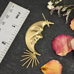 May include: Gold crescent moon earring with a face and a sunburst design. The earring is about 2 inches long.