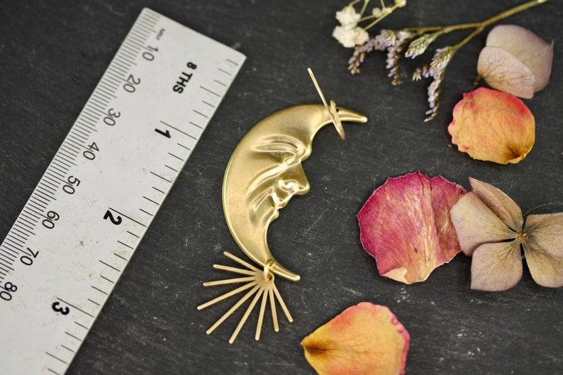 May include: Gold crescent moon earring with a face and a sunburst design. The earring is about 2 inches long.