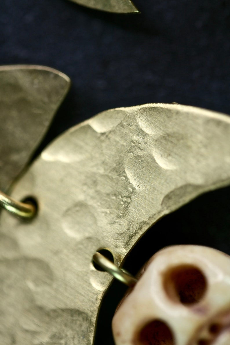 May include: Close-up of a gold crescent moon-shaped earring with a textured surface. The earring is attached to a white bone-like bead.
