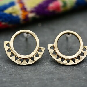 May include: A pair of gold-toned earrings with a hammered finish. Each earring features a circle with a half-circle of triangular cutouts around the bottom.