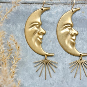 May include: A pair of gold-toned earrings featuring a crescent moon design with a face and a sunburst dangle.