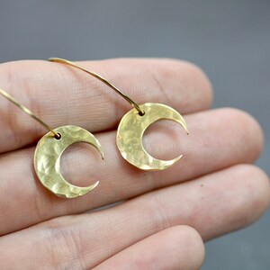 May include: A pair of gold-colored crescent moon earrings. The earrings have a hammered texture and are suspended from delicate, curved wires. The design is simple and elegant, suitable for everyday wear or special occasions.