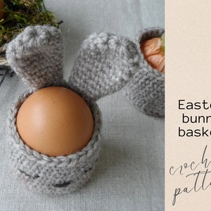 May include: A crochet Easter bunny basket with long floppy ears, made in a light gray color, holding a brown egg. The basket is a great way to decorate for Easter and can be used to hold small gifts or treats.