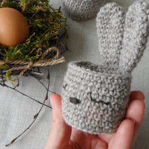 May include: A gray crocheted bunny egg holder with long floppy ears. The holder is designed to hold a single egg.