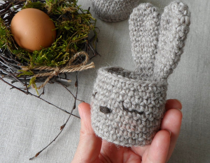 May include: A gray crocheted bunny egg holder with long floppy ears. The holder is designed to hold a single egg.