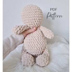 Könnte beinhalten: Ein beige gehäkelter Puppenkörper mit rundem Kopf, Armen und Beinen. Die Puppe wird in einer Hand gehalten. Der Text "PDF Pattern" ist kursiv auf der rechten Seite des Bildes geschrieben.