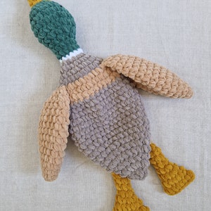 May include: A crocheted plush duck toy with a green head, brown and beige body, and yellow feet.