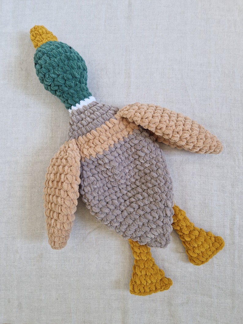 May include: A crocheted plush duck toy with a green head, brown and beige body, and yellow feet.