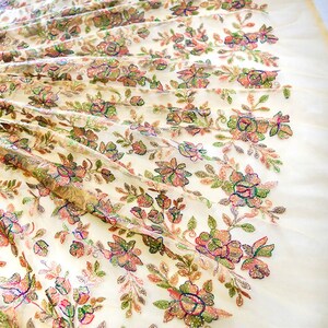 May include: White sheer fabric with a floral pattern embroidered with iridescent sequins. The flowers are in shades of pink, green, and brown.