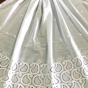 May include: White cotton fabric with a delicate paisley pattern embroidered around the edge. The fabric is sheer and has a soft, flowing texture.