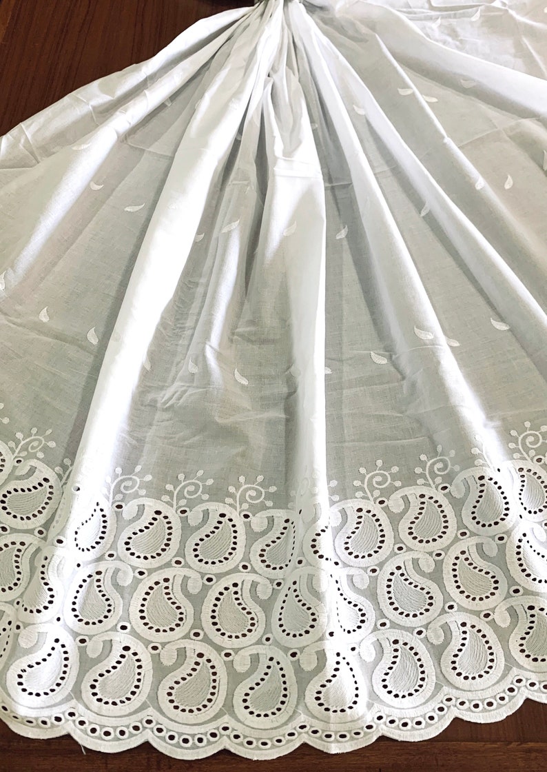 May include: White cotton fabric with a delicate paisley pattern embroidered around the edge. The fabric is sheer and has a soft, flowing texture.