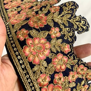 May include: Navy blue embroidered trim with gold and pink floral designs. The trim has a scalloped edge and a row of gold sequins.