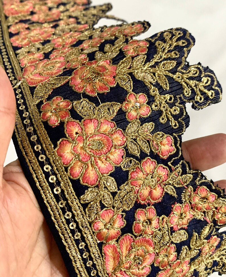 May include: Navy blue embroidered trim with gold and pink floral designs. The trim has a scalloped edge and a row of gold sequins.